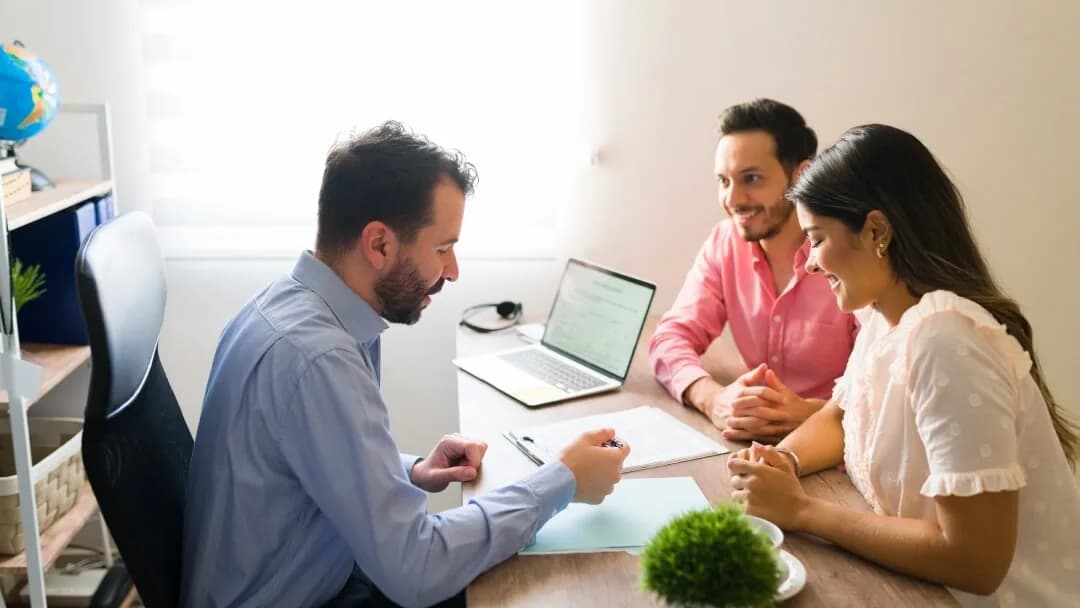 Un couple souriant discute avec un conseiller financier lors d'une réunion dans un bureau