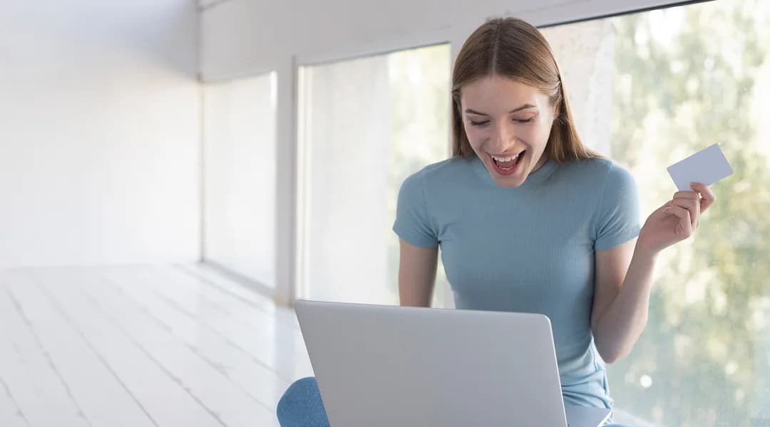 Femme enthousiaste tenant une carte de crédit devant son ordinateur après avoir obtenu un prêt en ligne rapidement