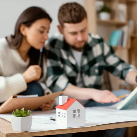 Couple consulting financial documents beside a house model when considering an urgent loan for household expenses