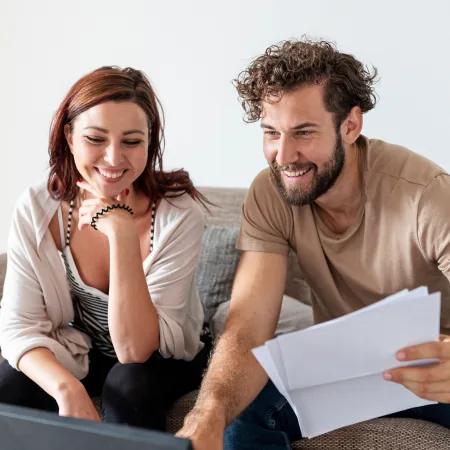 Couple smiling while reviewing household expense documents together on a laptop at home