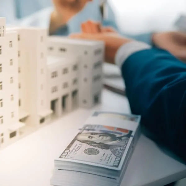 Liasse de billets posée devant un modèle d'immeuble illustrant la rapidité et la simplicité du processus de Prêt Urgent