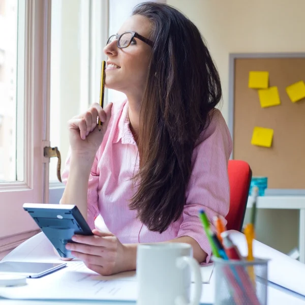 Une femme portant des lunettes est assise à un bureau avec une calculatrice devant elle.