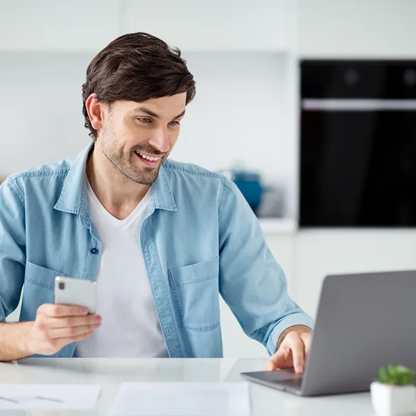 Homme souriant utilisant un ordinateur et un téléphone pour gérer son prêt d'argent de manière responsable