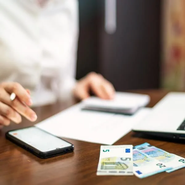 Une personne utilise son téléphone pour gérer ses finances avec des billets de banque posés sur le bureau.