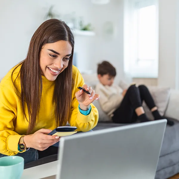 Femme souriante consultant son téléphone et son ordinateur pour effectuer une demande de prêt en ligne au Québec
